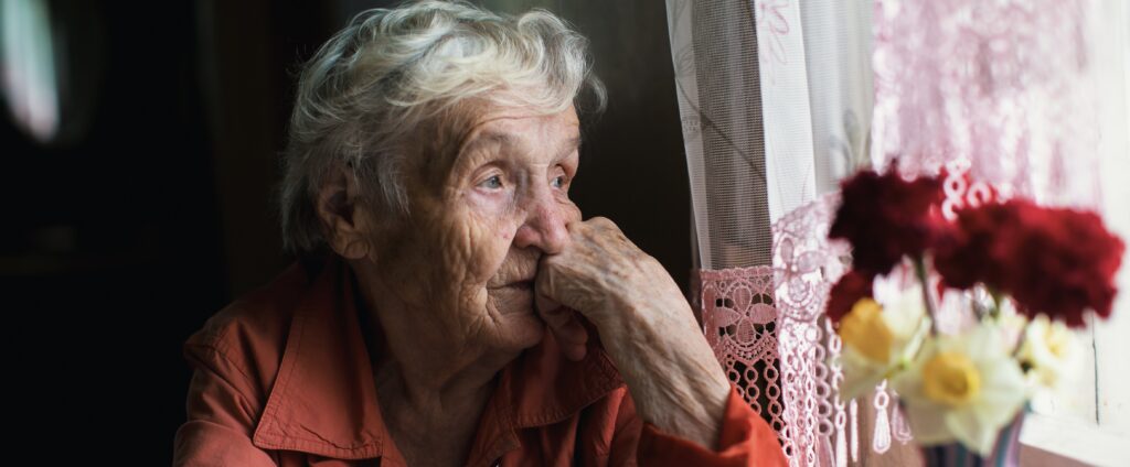 Elderly woman looks sadly out the window.